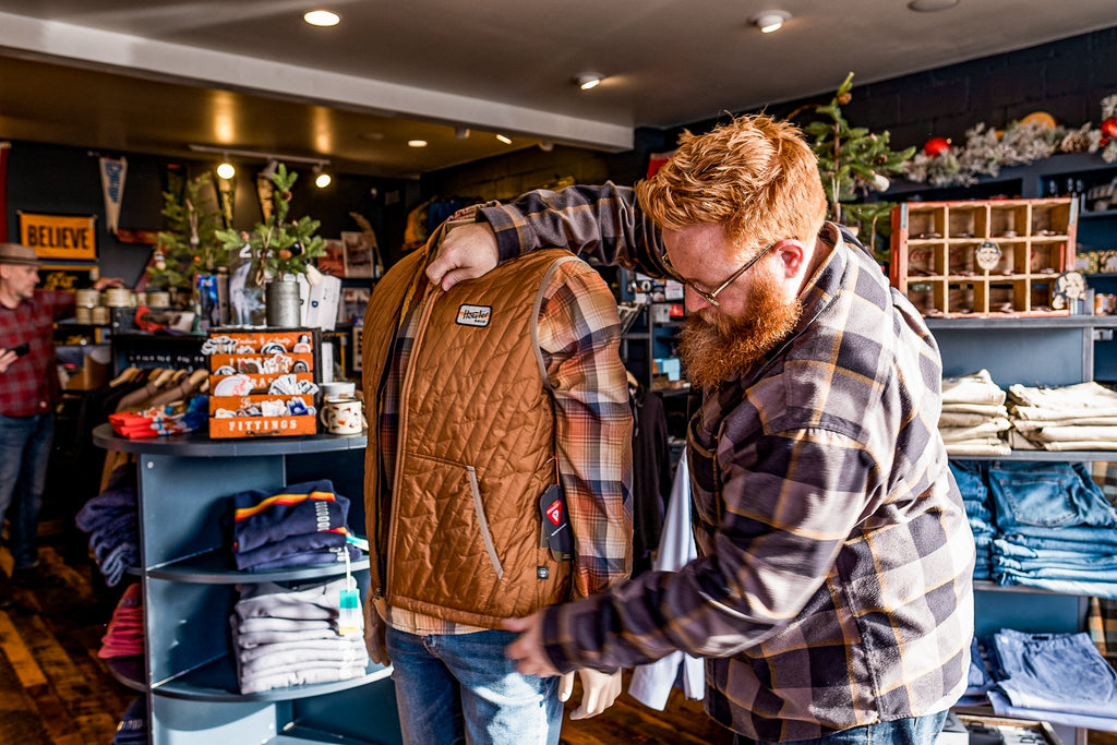 A retail storekeeper dresses a mannequin with a voltage quilted vest from Howler Brothers Clothing company.