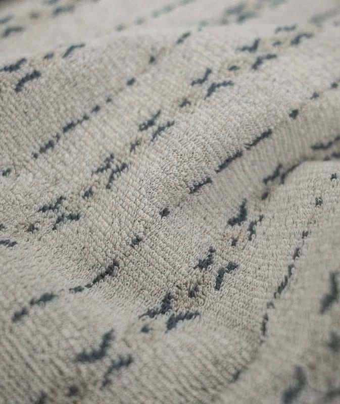 Close-up view of tan knit fabric with jacquard texture and subtle dark woven pattern, highlighting the soft, looped cotton-spandex blend.