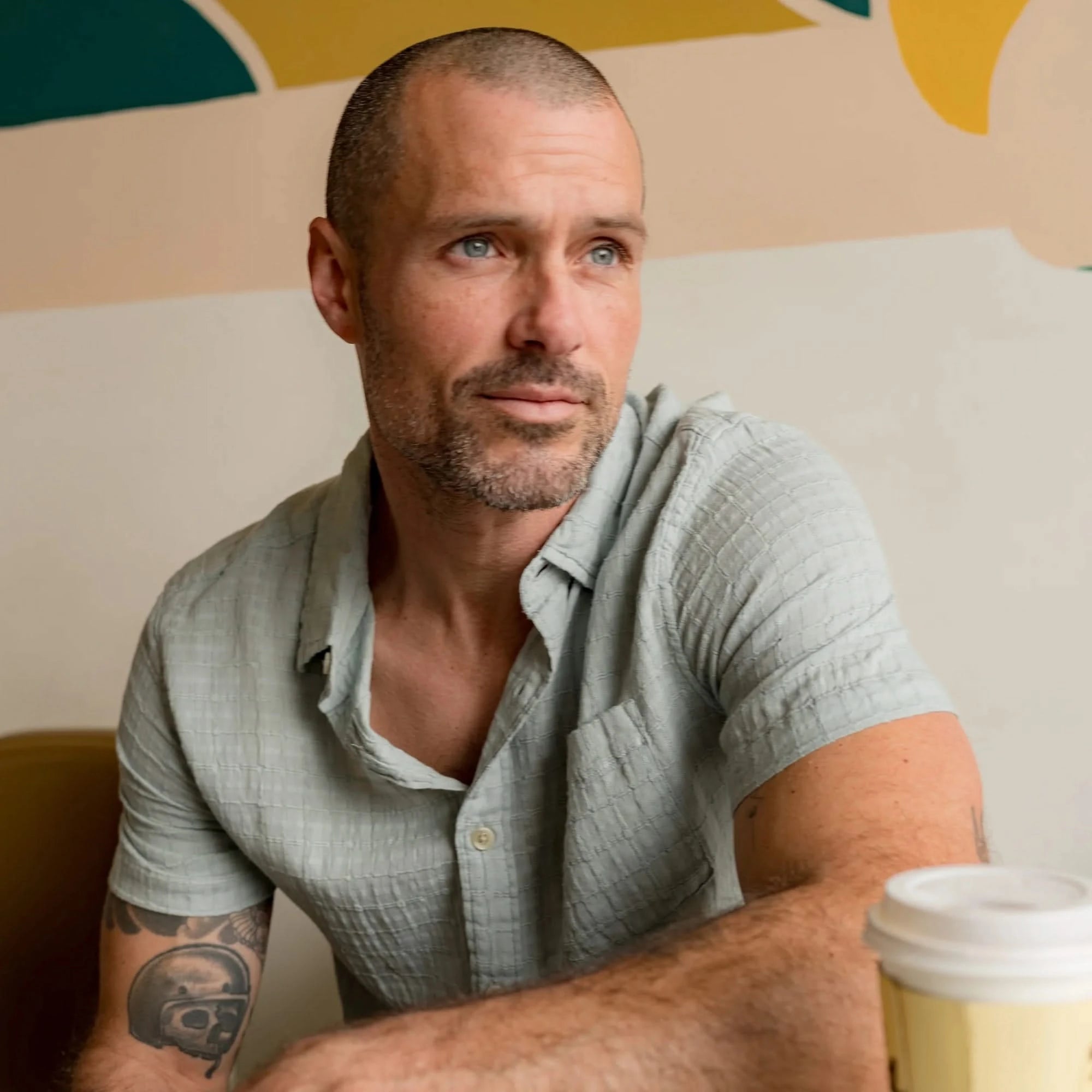 Man wearing the Bamboo Dobby Short Sleeve Shirt in Abyss green, seated indoors with a coffee cup, showcasing the relaxed fit and breathable texture.