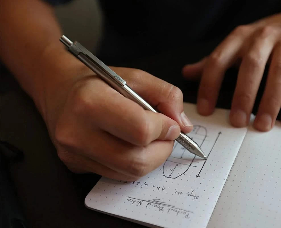 The James Brand Burwell Pen in stainless with Model writing in a notebook