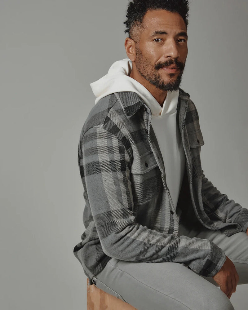 Model seated wearing Generation Plaid Shirt in grey over white hoodie and light grey pant