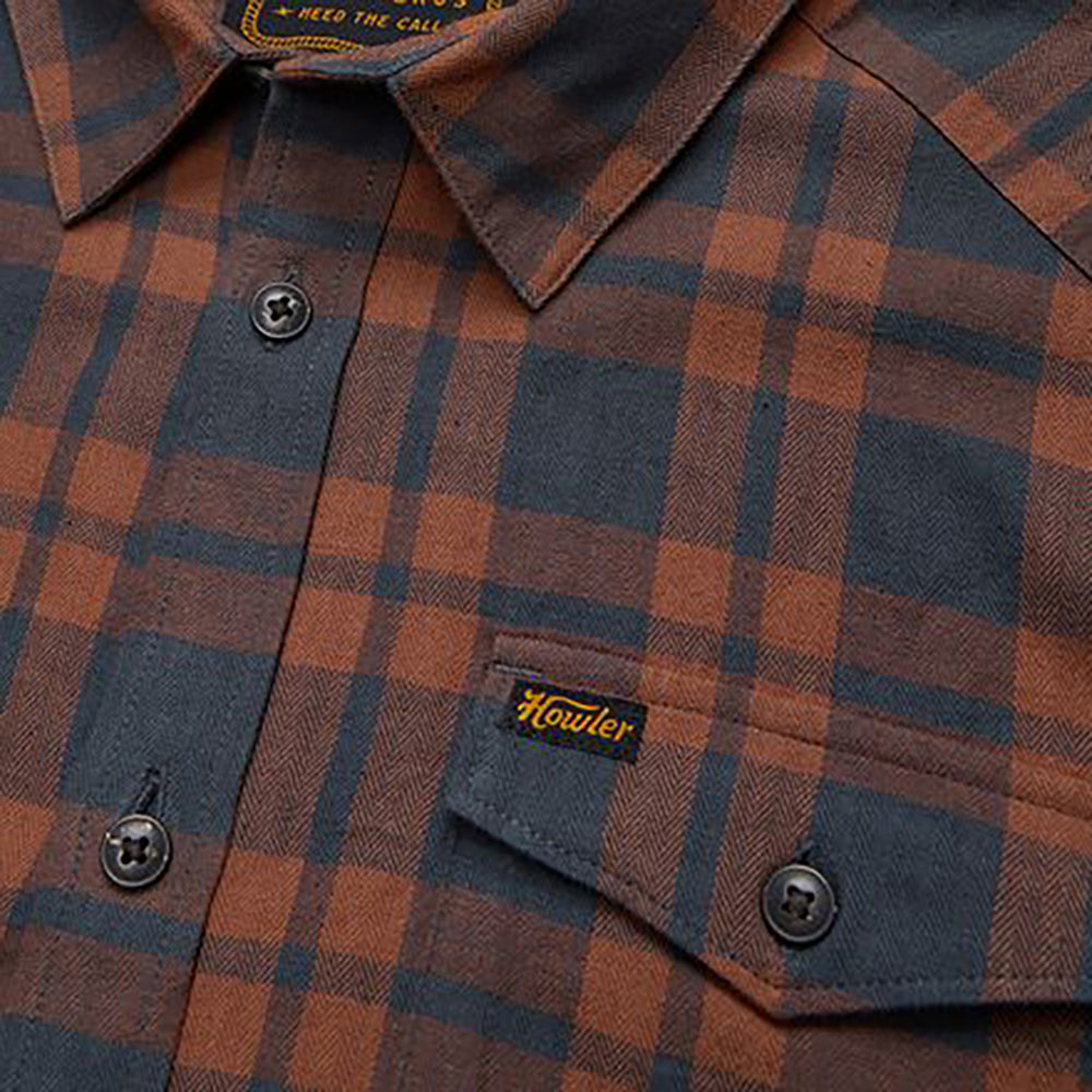 Zoomed-in view of Howler Brothers logo on chest pocket of La Grange Flannel Shirt in rust and navy plaid