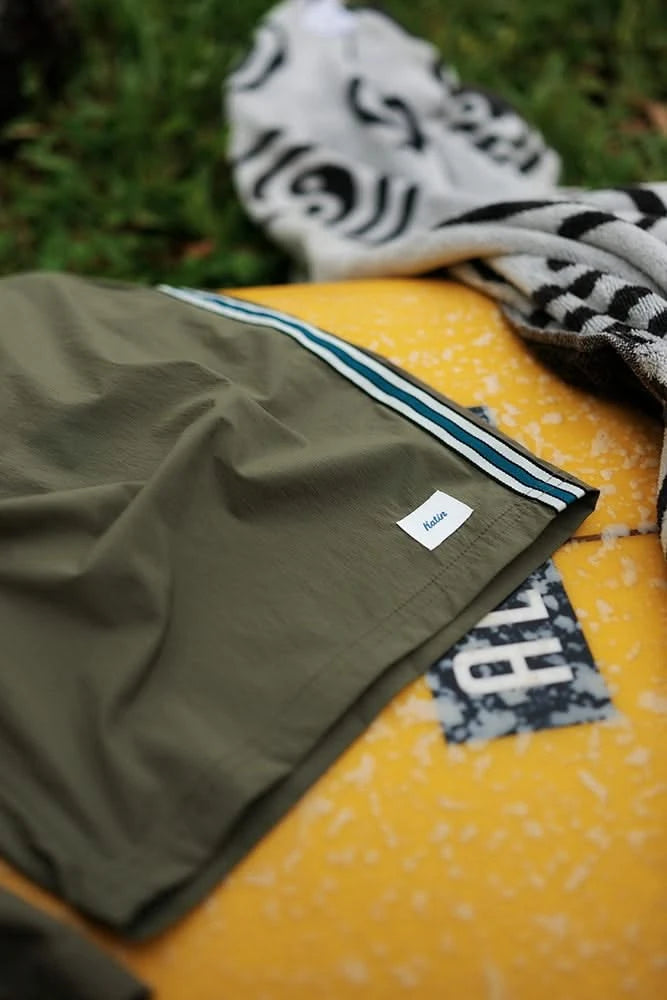 Close-up of Theo swim trunk on yellow surfboard showing side stripe detail – men's beachwear at The Simple Man Omaha
