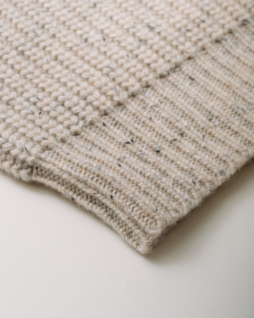 Close-up detail of wool blend Donegal sweater ribbed hem in off-white