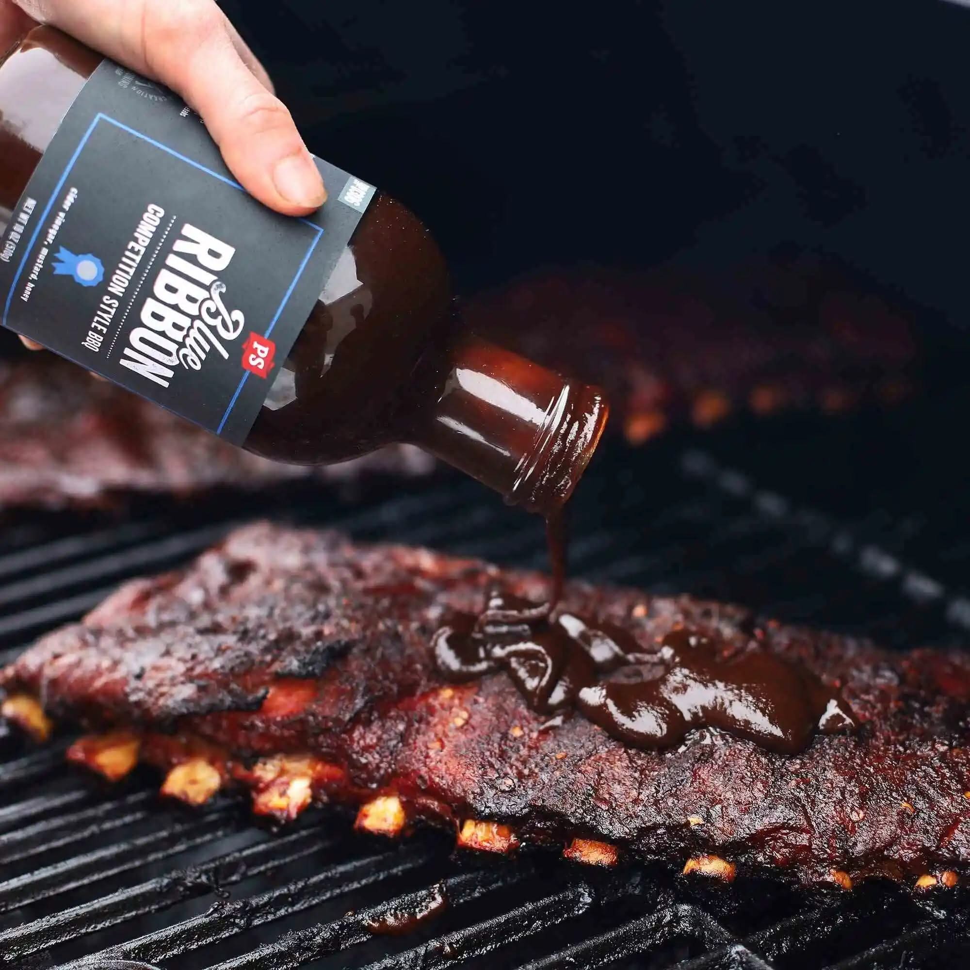 Hand pouring Blue Ribbon BBQ Sauce over ribs on a grill – thick, smoky competition-style sauce made for slow-smoked meats and backyard BBQ pros.
