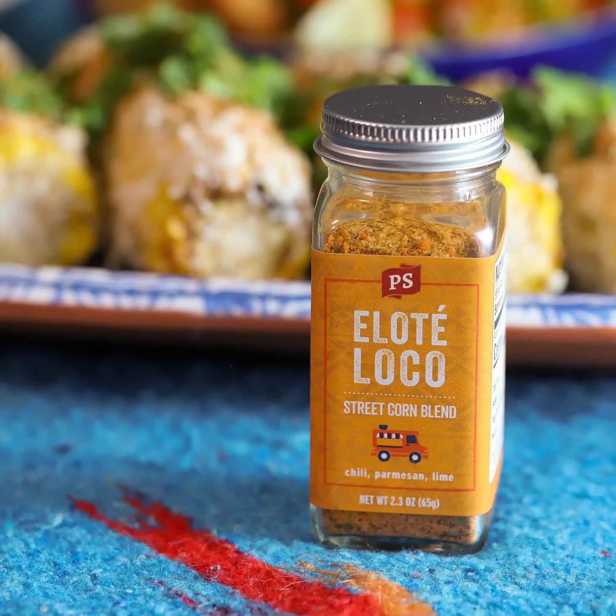Close-up of Elote Loco street corn seasoning jar by PS Seasoning, surrounded by grilled Mexican-style corn on a colorful serving platter.
