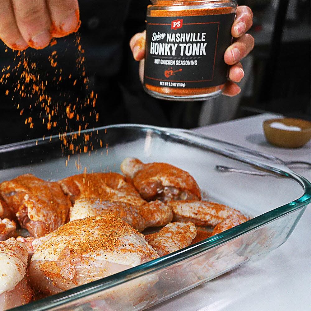 Person seasoning raw chicken with Nashville Hot Chicken Rub in a glass baking dish – spicy honky tonk rub for grilling, frying, and BBQ recipes.