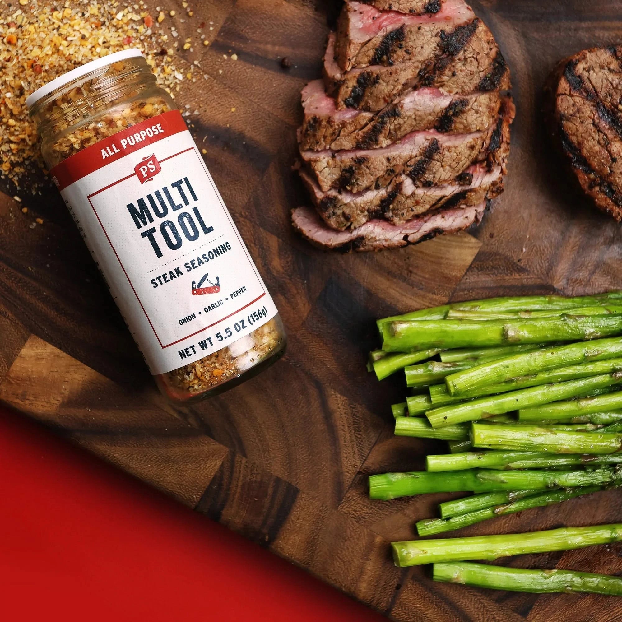 Multi-Tool All Purpose Seasoning on cutting board with grilled steak and asparagus