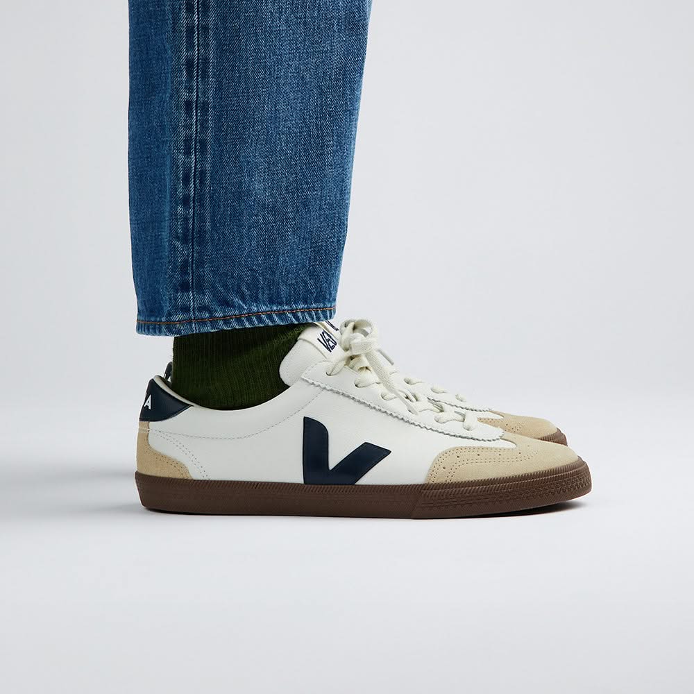 Model wearing VEJA Volley men's sneakers in white organic leather with navy logo, tan suede accents, and brown rubber sole – available at The Simple Man." Side view