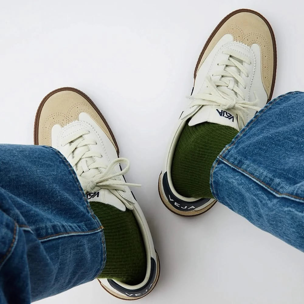 Model wearing VEJA Volley men's sneakers in white organic leather with navy logo, tan suede accents, and brown rubber sole – available at The Simple Man." Top down view