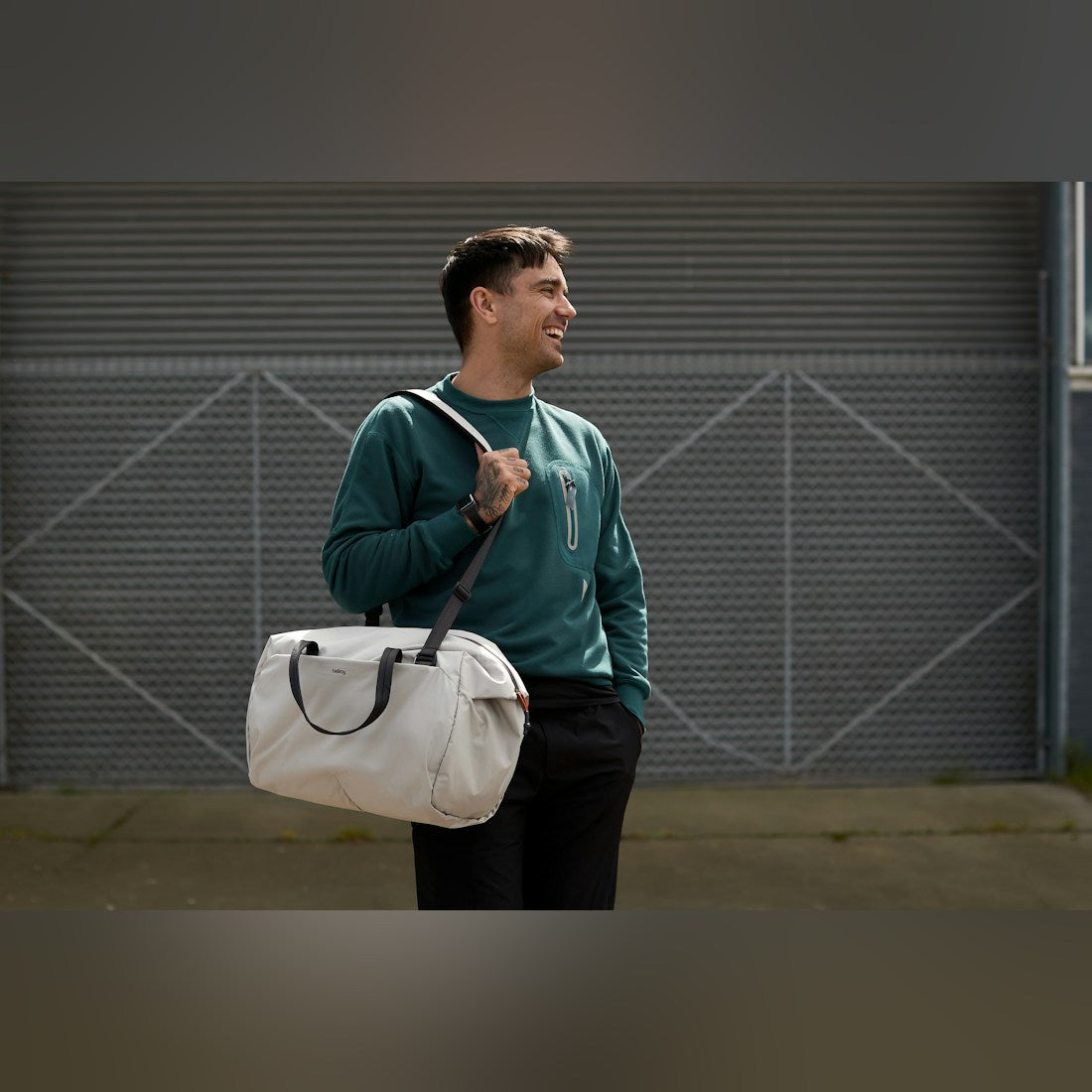 Bellroy Lite Duffel in Ash, carried over the shoulder by a smiling man - The Simple Man