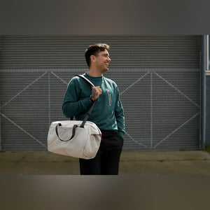 Bellroy Lite Duffel in Ash, carried over the shoulder by a smiling man - The Simple Man