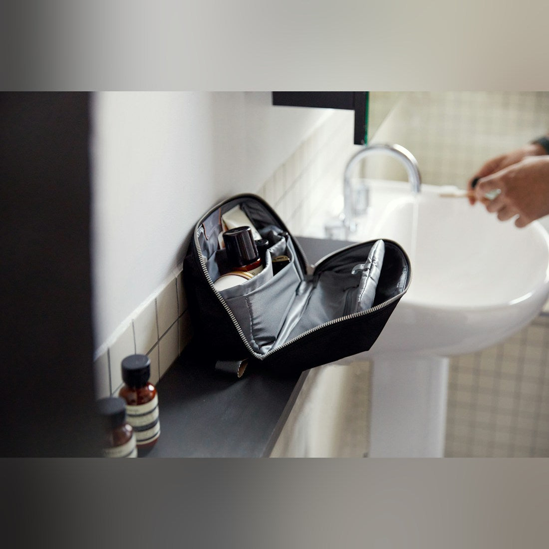 Bellroy Toiletry Kit Plus in Black, open on the edge of a bathroom sink with toiletries inside - The Simple Man