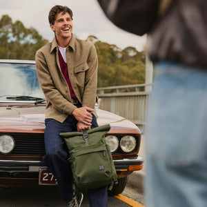 Bellroy Classic Rolltop commuter backpack in Olive, worn by a man sitting on a car - The Simple Man