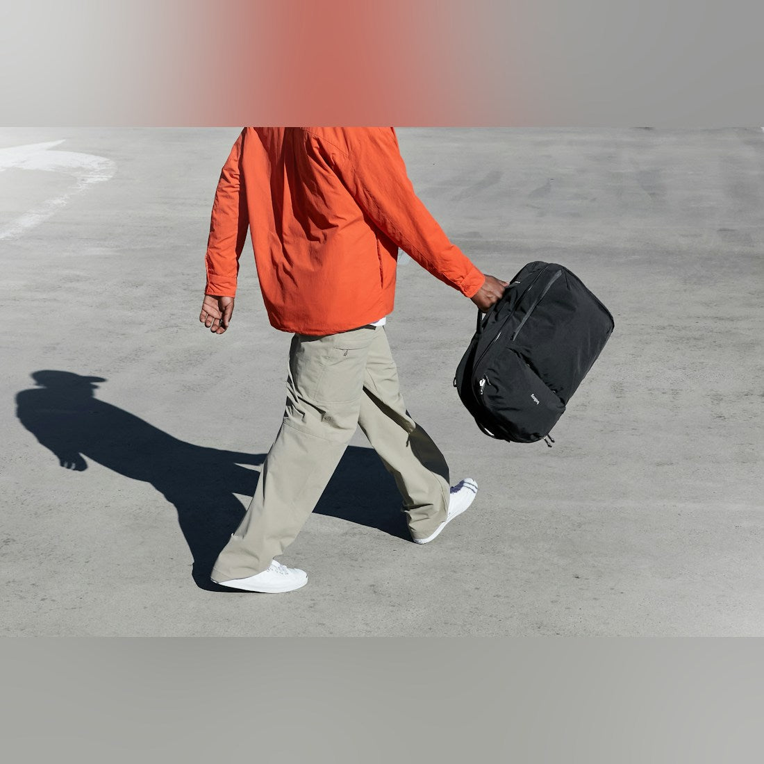 Bellroy Lite Travel Pack 38L in Black, carried by the handle by a man walking - The Simple Man