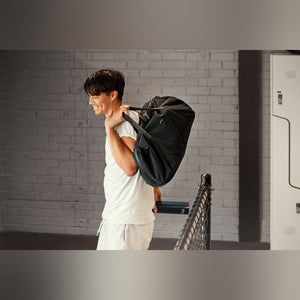 Bellroy Venture Duffel 40L in Black, carried over the shoulder by a man walking past a building - The Simple Man