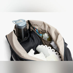 Bellroy Lite Duffel in Black, open with a water bottle and sneakers inside - The Simple Man