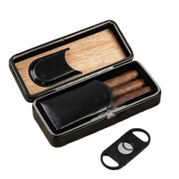 Black leather folding cigar travel case open with three cigars and double-blade guillotine cutter on wood surface