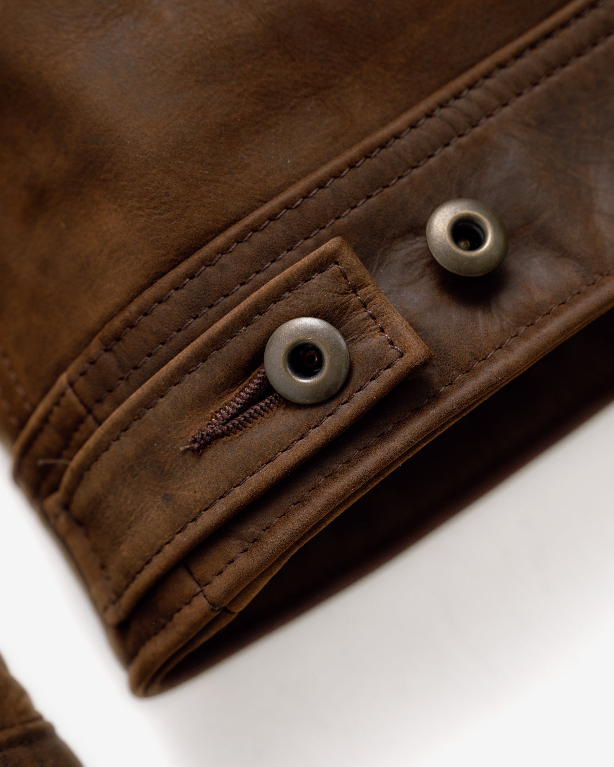 Close-up of the metal shank button side tab on the brown cowhide trucker jacket - The Simple Man