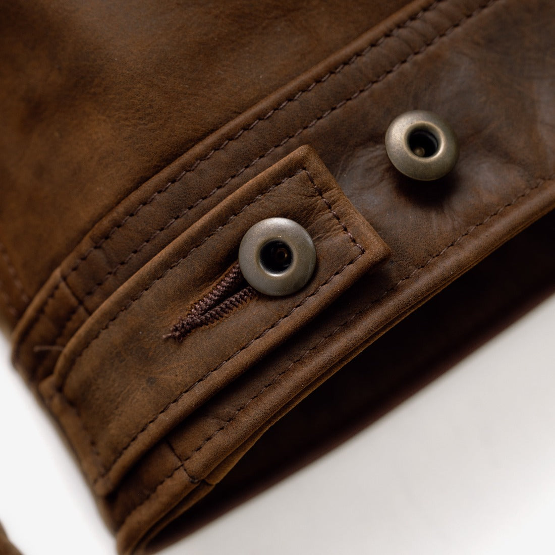 Close-up of the metal shank button side tab on the brown cowhide trucker jacket - The Simple Man
