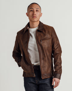 Man wearing the brown cowhide trucker jacket open over a white tee and dark jeans - The Simple Man