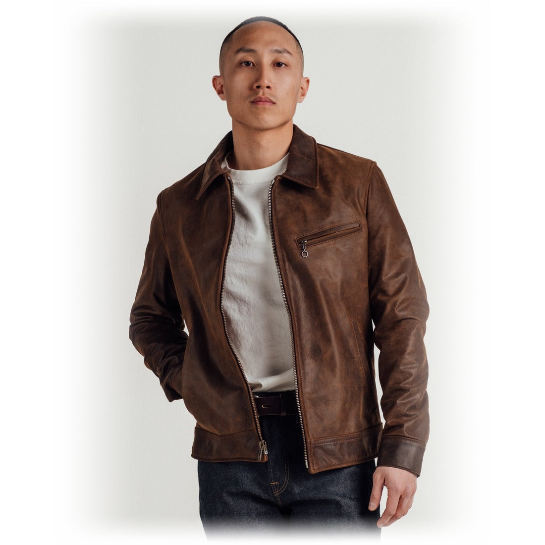 Man wearing the brown cowhide trucker jacket open over a white tee and dark jeans - The Simple Man