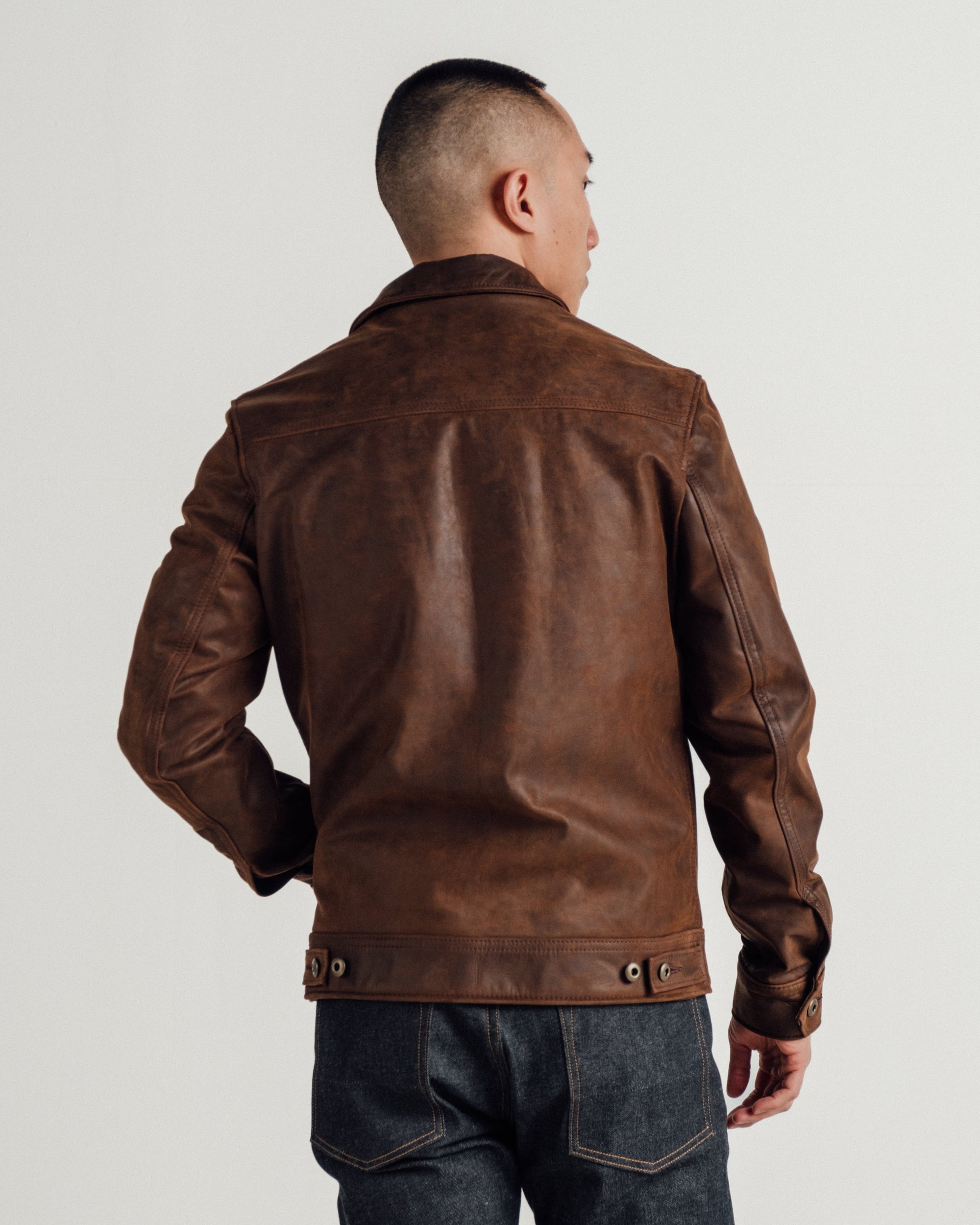 Back view on model of the brown cowhide trucker jacket with adjustable side tabs - The Simple Man