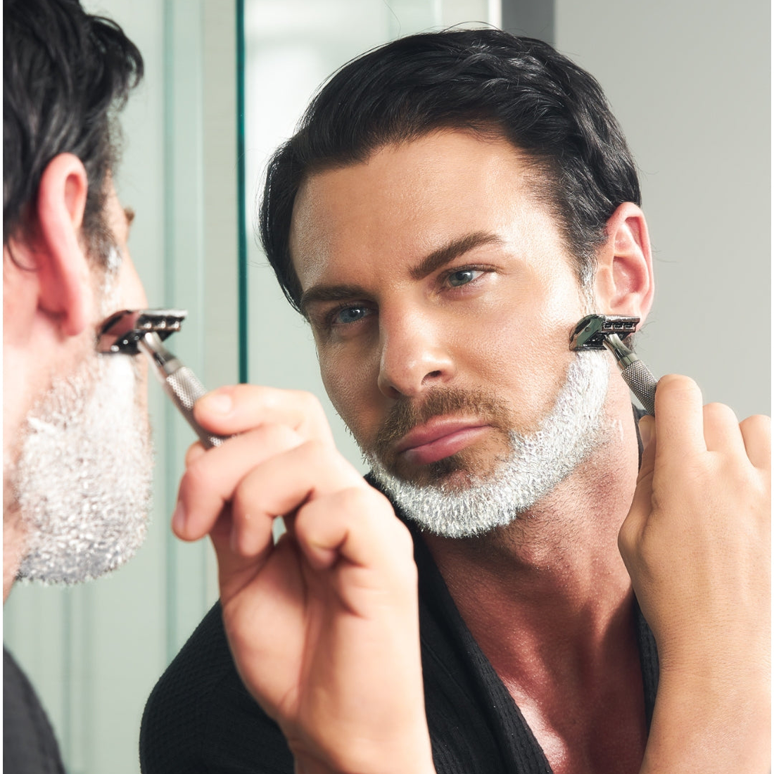 Two men shaving with safety razors in front of a bathroom mirror, lifestyle shot