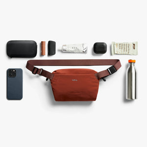 Bellroy Lite Sling Mini in Clay, flat lay of everyday items with the bag worn on a belt - The Simple Man