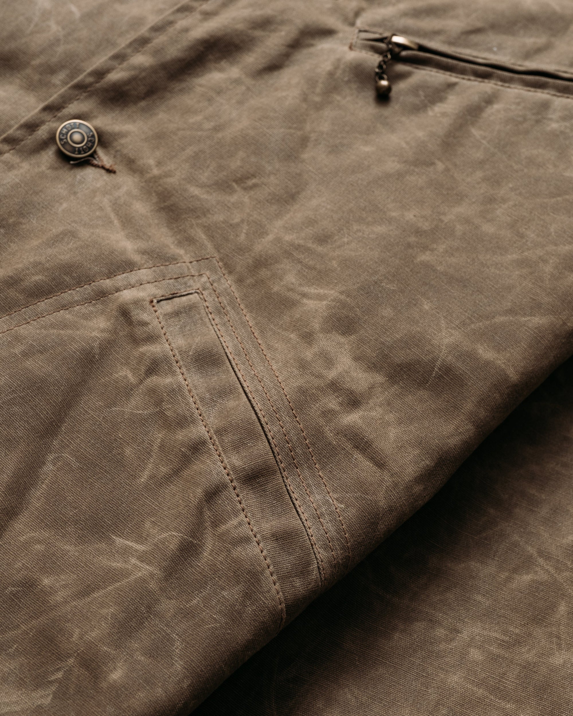 Close-up of the lower diagonal welt pocket and waxed cotton texture on the brown mechanic jacket - The Simple Man