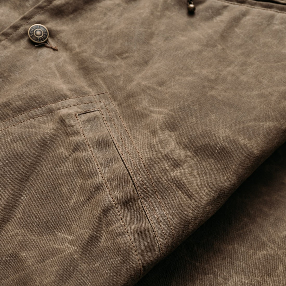 Close-up of the lower diagonal welt pocket and waxed cotton texture on the brown mechanic jacket - The Simple Man
