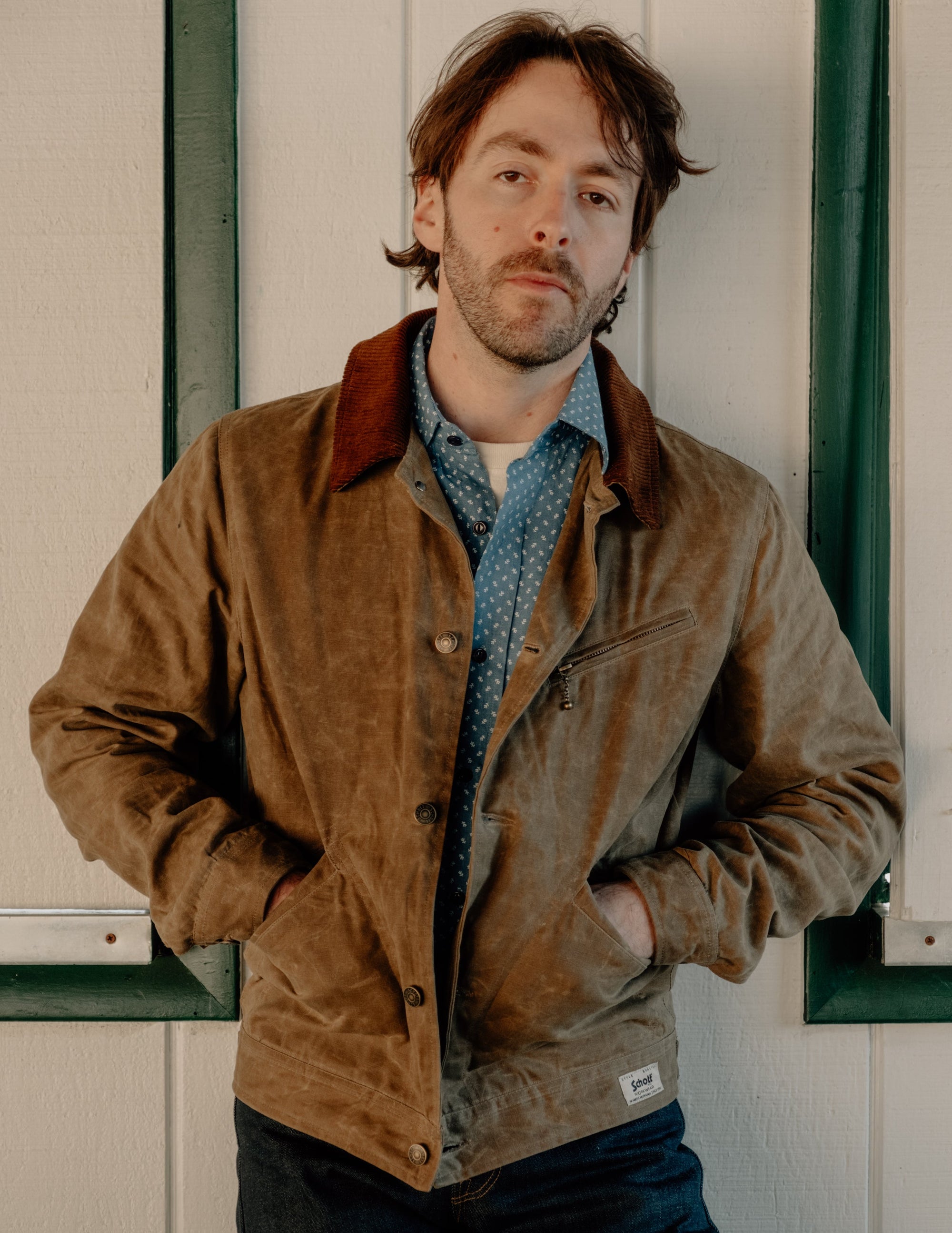 Man wearing the brown waxed cotton mechanic jacket with hands in pockets over a chambray shirt - The Simple Man