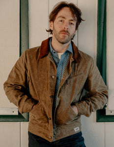 Man wearing the brown waxed cotton mechanic jacket with hands in pockets over a chambray shirt - The Simple Man