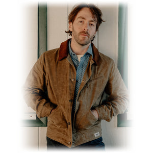 Man wearing the brown waxed cotton mechanic jacket with hands in pockets over a chambray shirt - The Simple Man