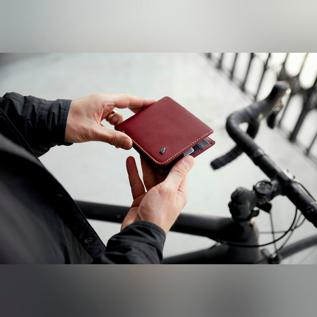 Bellroy Hide & Seek RFID leather wallet, shown in burgundy and held in both hands near bicycle handlebars - The Simple Man