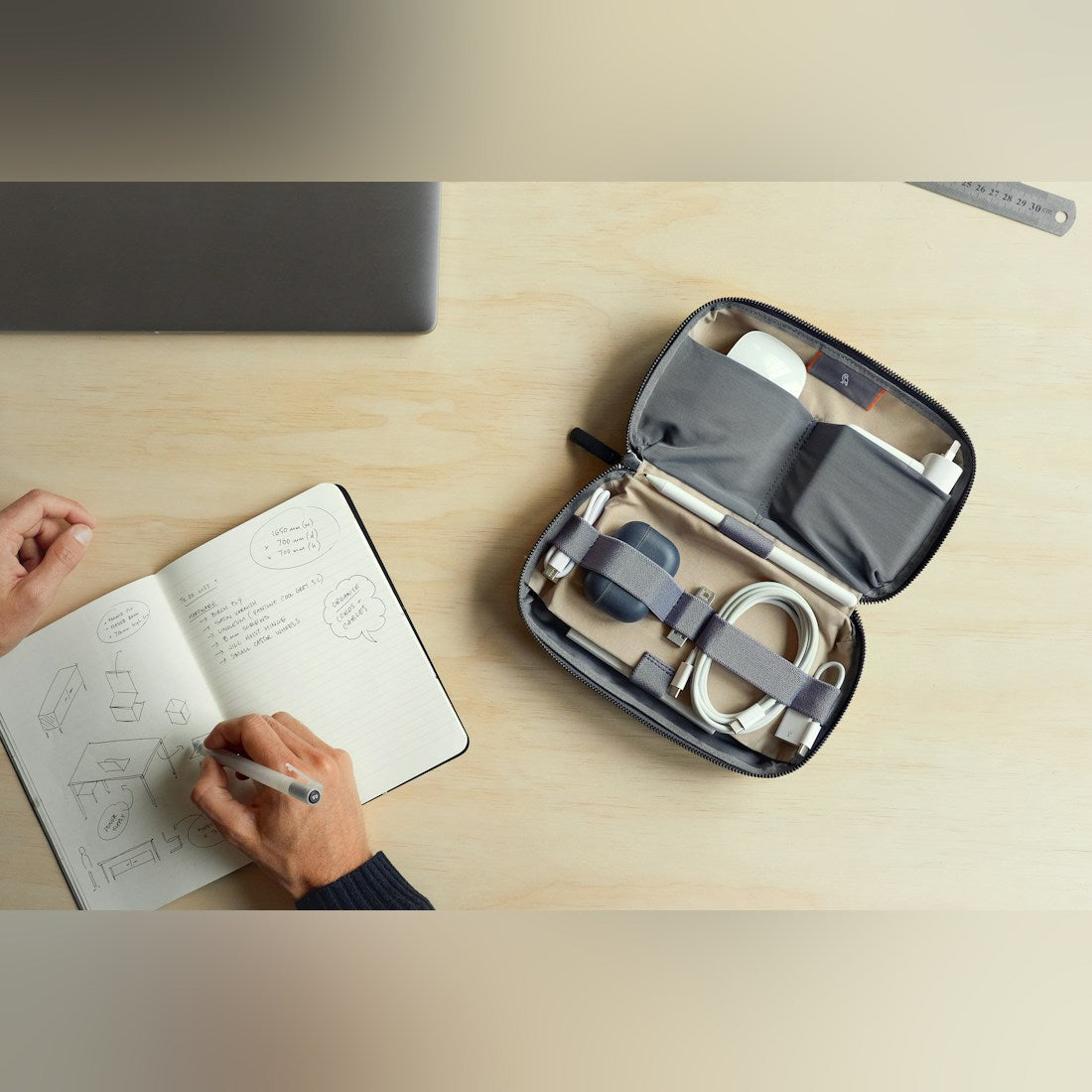 Bellroy Tech Kit cable organizer, open with cables and chargers on a desk beside a notebook - The Simple Man