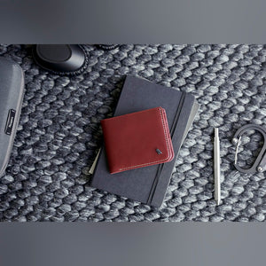 Bellroy Hide & Seek RFID leather wallet, shown in burgundy on a textured grey mat beside a notebook and pen - The Simple Man