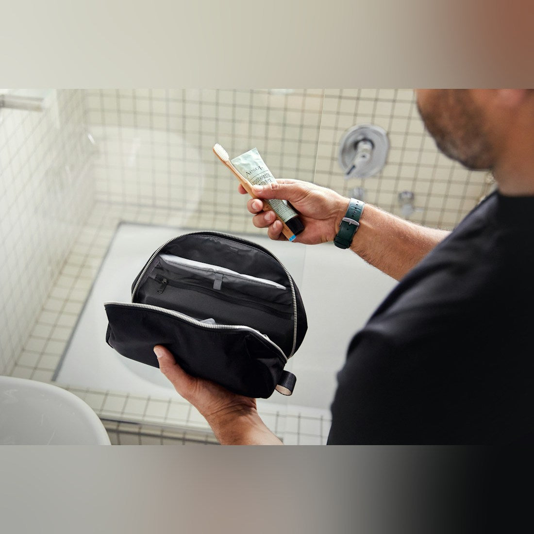 Bellroy Toiletry Kit Plus in Black, held open beside a bathroom sink - The Simple Man