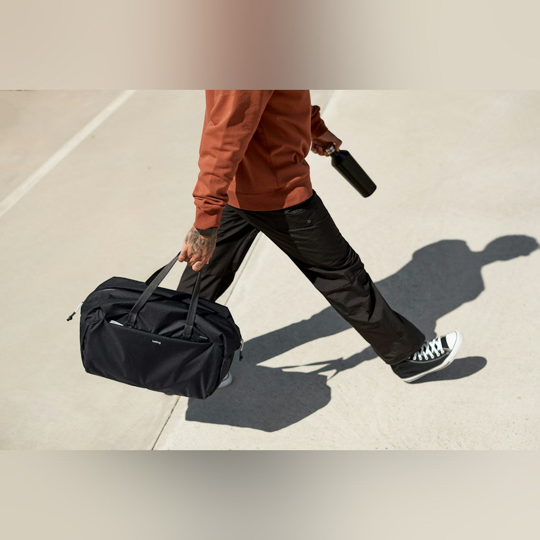 Bellroy Lite Duffel in Black, carried over the shoulder by a man walking down a sunlit street - The Simple Man