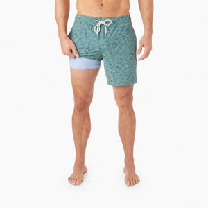 Model Wearing Fair Harbor Bayberry swim Trunk in Green Mini Floral, Front View with legged pulled up showing the liner