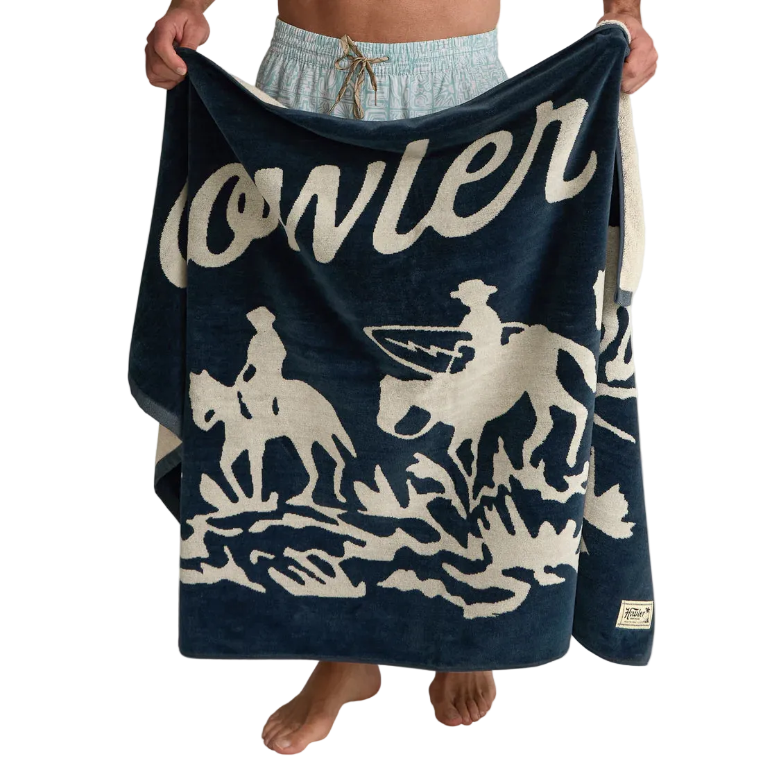 Man holding Howler Bros Posse Beach Towel open showing full graphic – midnight navy cream cowboy surfer artwork heavyweight cotton beach towel