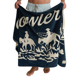 Man holding Howler Bros Posse Beach Towel open showing full graphic – midnight navy cream cowboy surfer artwork heavyweight cotton beach towel