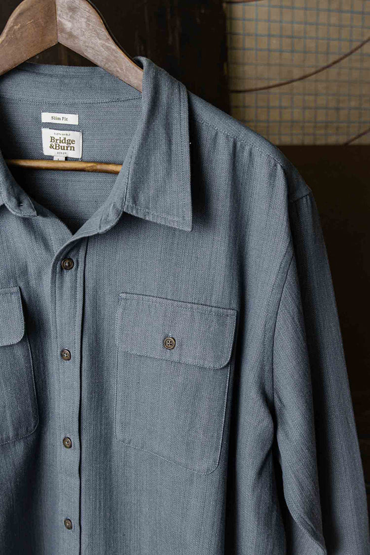 Close-up of denim herringbone Bedford Shirt collar and chest pockets on hanger.