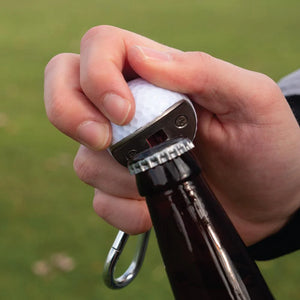 Golf Ball Bottle opener, with carabiner clip, shown opening a bottle with model hand