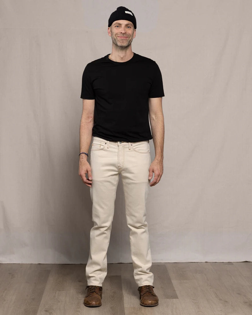 Man wearing Ace Rivington Brodie Taper Jean in Ecru Rinse with black t-shirt and beanie — full front view men's tapered denim