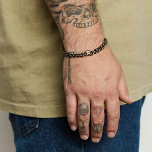 Man wearing a brass work patina chain bracelet on wrist, shown with tattoos and casual outfit, Studebaker Metals at The Simple Man.