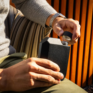 Matte black Cool Flask being opened by man in casual fall outfit – durable stainless steel pocket flask from The Simple Man.