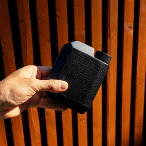 Man holding matte black Cool Flask outdoors against wooden background – slim stainless steel pocket flask from The Simple Man.