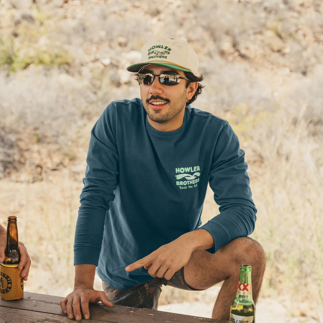 Man wearing Howler Brothers Flocka Seagulls long sleeve shirt in Key Largo blue, sitting outdoors with sunglasses and a beer, casual fall outfit