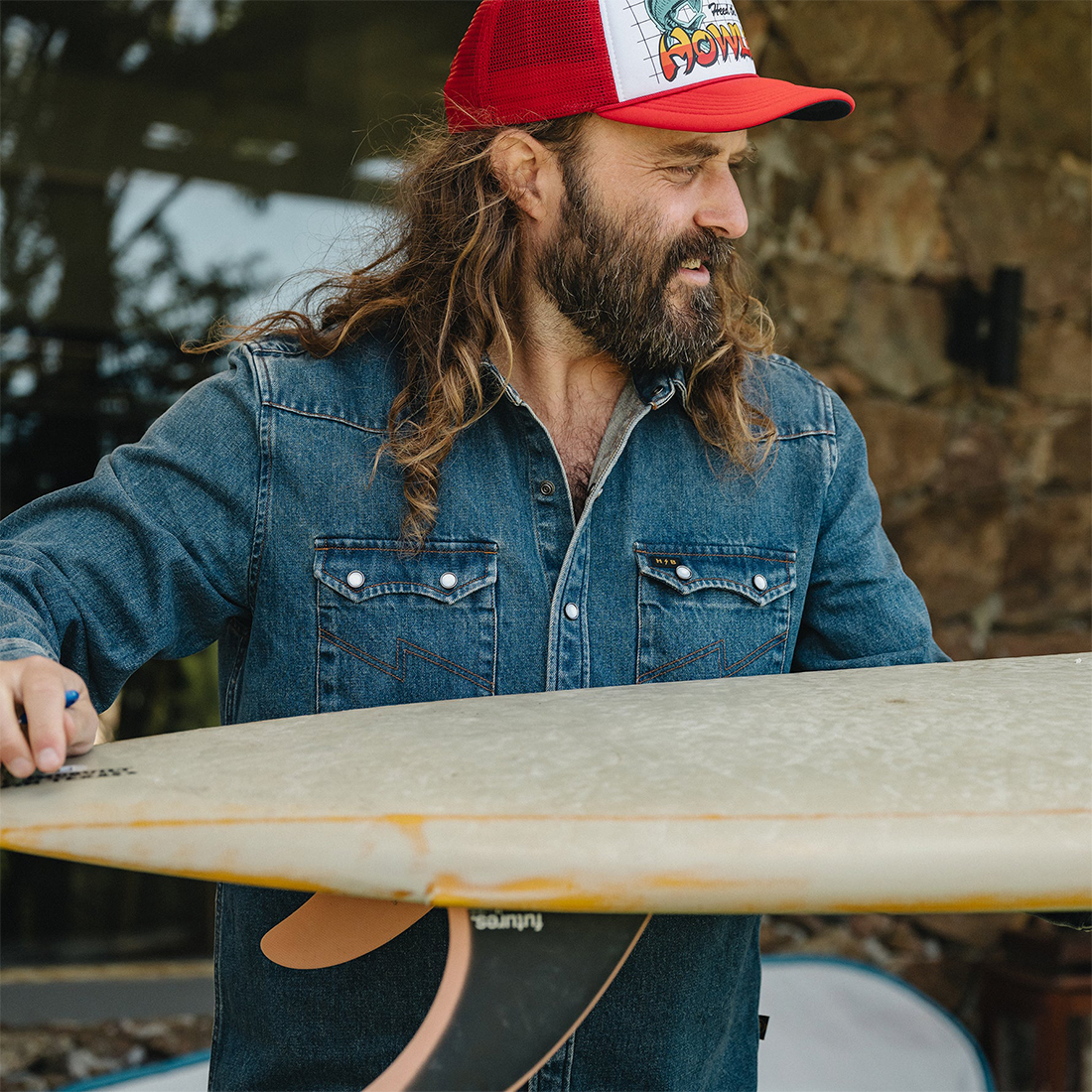 Man in a trucker hat working on a surfboard in the Dust Up Denim Snapshirt, worn open at the collar, lifestyle shot